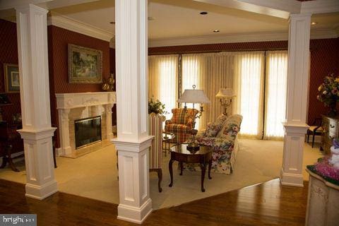 sitting room featuring ornate columns, wood finished floors, crown molding, and a high end fireplace