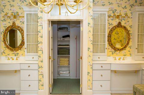 bathroom featuring a sink, two vanities, and wallpapered walls