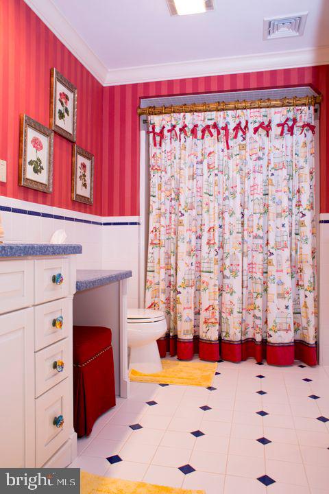 bathroom featuring toilet, ornamental molding, wainscoting, vanity, and wallpapered walls