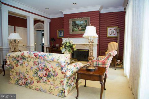 carpeted living room with wallpapered walls, a fireplace, and crown molding