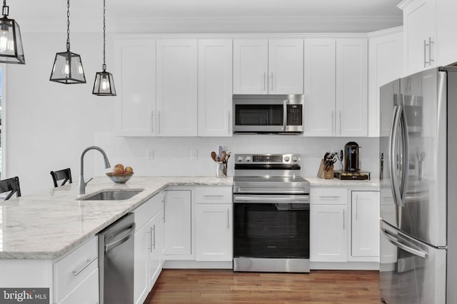 kitchen featuring stainless steel appliances, white cabinetry, a sink, wood finished floors, and a peninsula