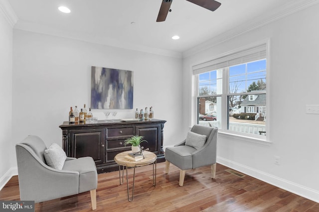 sitting room with recessed lighting, wood finished floors, baseboards, ornamental molding, and a dry bar