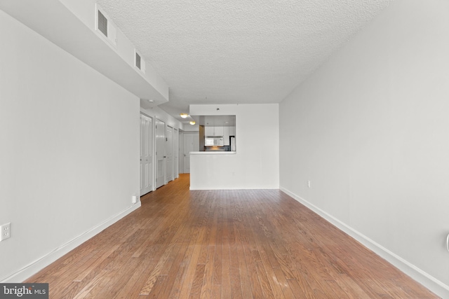 unfurnished living room with baseboards, wood-type flooring, and a textured ceiling