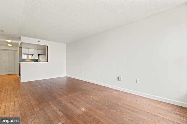 unfurnished living room featuring baseboards, a textured ceiling, and light wood finished floors