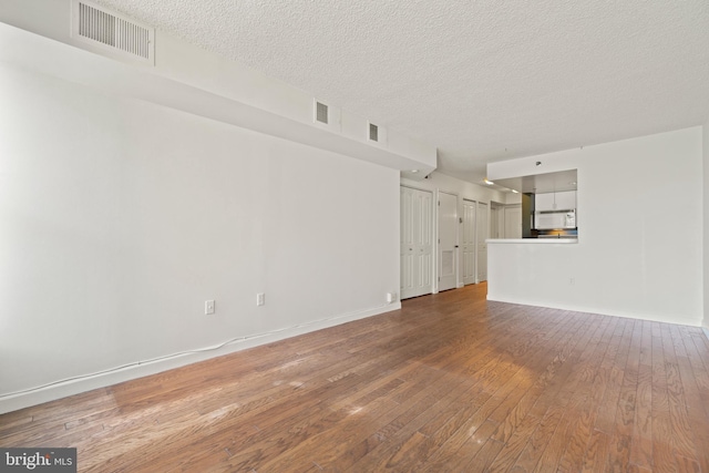 unfurnished living room featuring hardwood / wood-style floors, baseboards, visible vents, and a textured ceiling