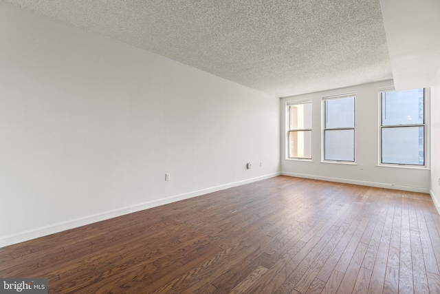 spare room with dark wood-type flooring, baseboards, and a textured ceiling