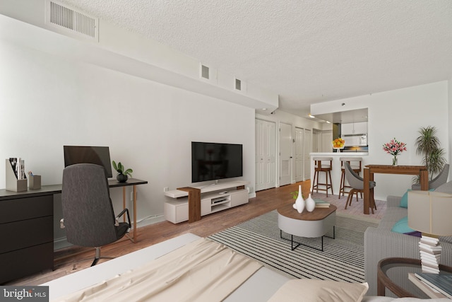 living room with visible vents, baseboards, a textured ceiling, and wood finished floors