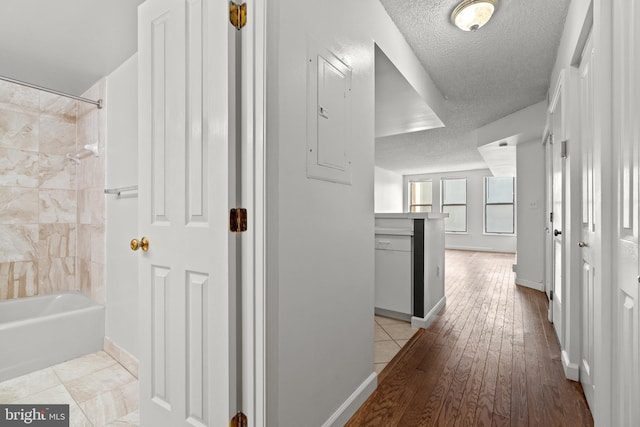 hallway featuring baseboards, light wood-type flooring, and a textured ceiling