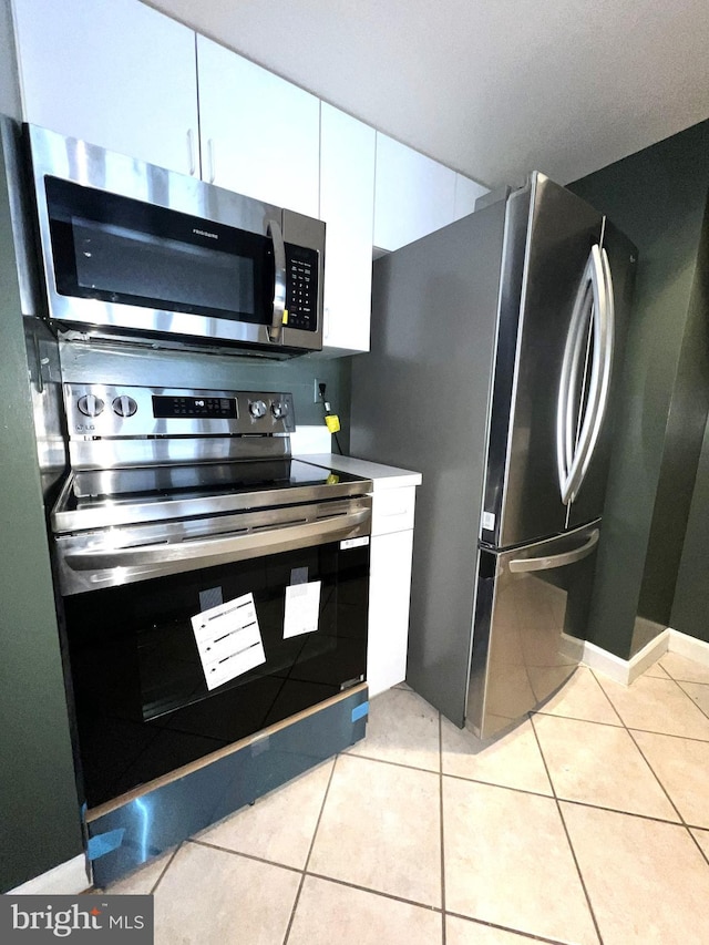 kitchen featuring light tile patterned floors, stainless steel appliances, baseboards, and white cabinets