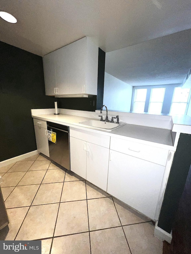 kitchen featuring light tile patterned floors, dishwashing machine, white cabinets, and a sink