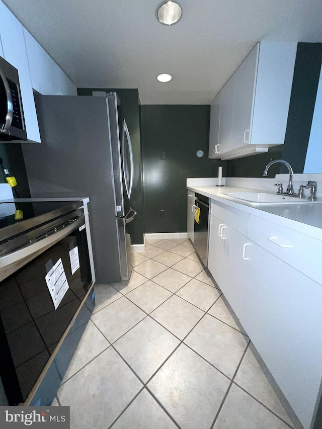 kitchen featuring light countertops, light tile patterned floors, white cabinets, black appliances, and a sink