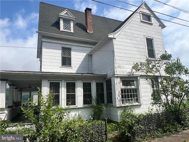 view of front of home featuring a shingled roof, a chimney, and a ceiling fan