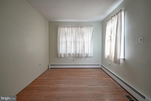 unfurnished room featuring baseboard heating, wood finished floors, and visible vents