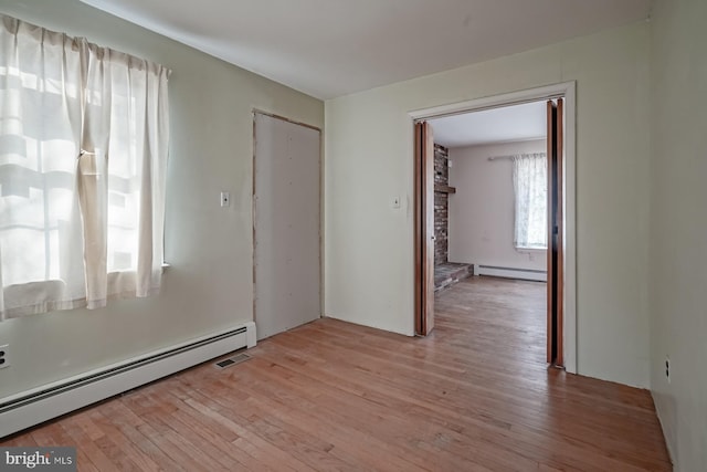 spare room featuring a baseboard radiator, a fireplace, and light wood-style flooring