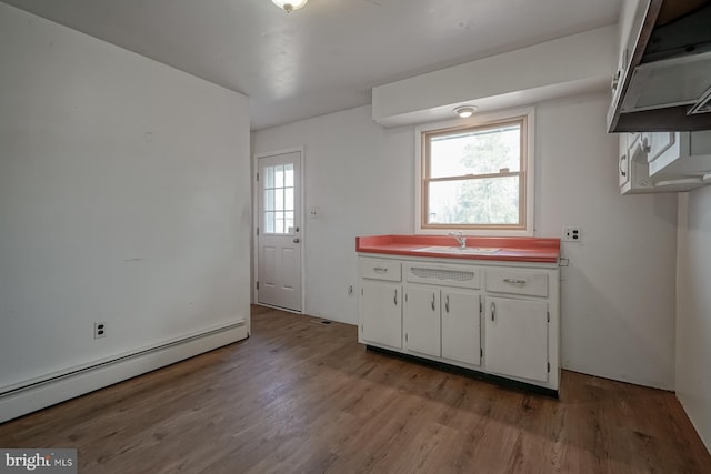 kitchen with white cabinets, baseboard heating, a sink, and wood finished floors