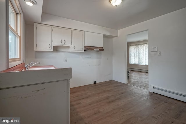 kitchen with baseboard heating, wood finished floors, white cabinetry, and under cabinet range hood