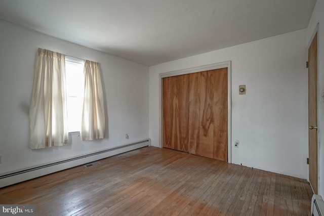 unfurnished bedroom featuring a closet, wood-type flooring, and baseboard heating