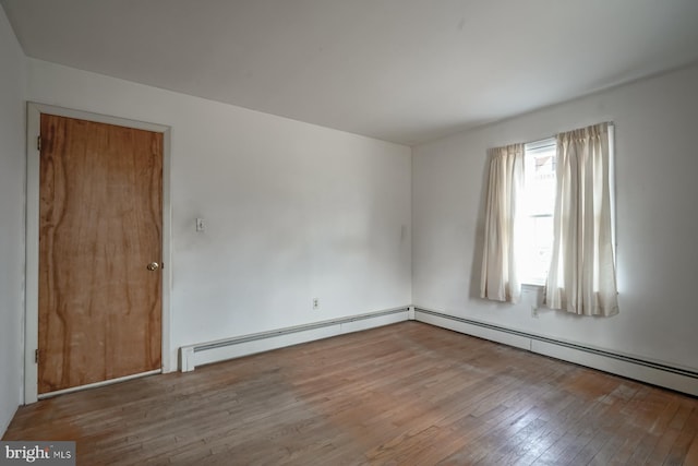 empty room featuring baseboard heating and wood-type flooring