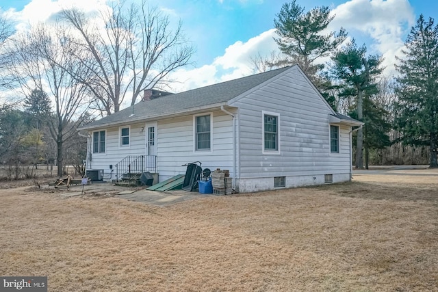 rear view of property featuring a yard, central AC unit, a chimney, and roof with shingles