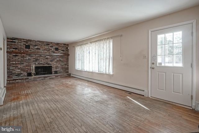 unfurnished living room featuring a baseboard heating unit, a brick fireplace, wood-type flooring, and a healthy amount of sunlight