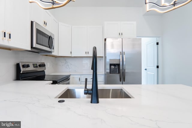 kitchen with stainless steel appliances, white cabinetry, a sink, and light stone counters