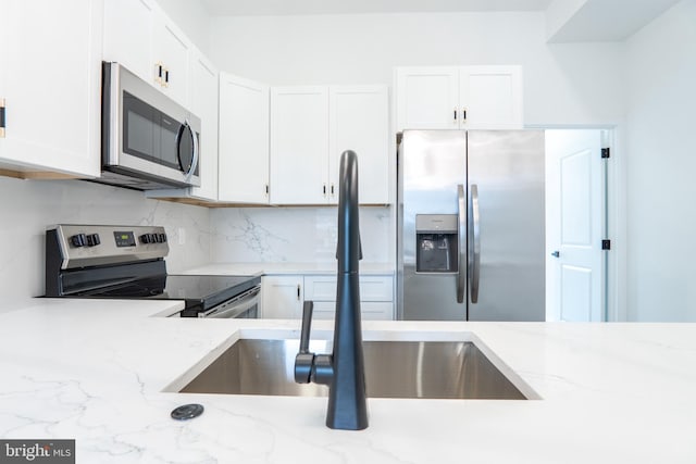 kitchen featuring white cabinets, light stone countertops, stainless steel appliances, and backsplash