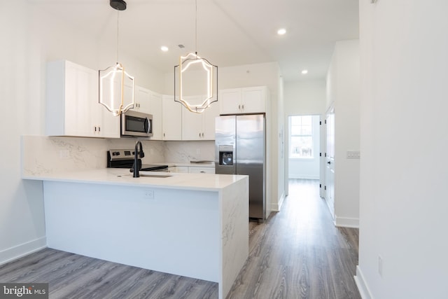 kitchen featuring a peninsula, white cabinets, light countertops, appliances with stainless steel finishes, and decorative light fixtures