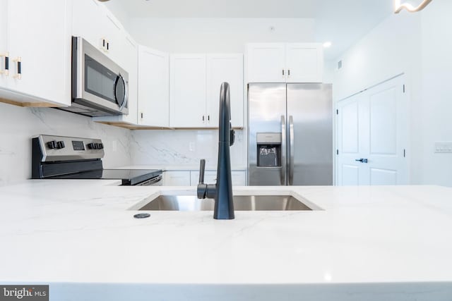 kitchen with stainless steel appliances, a sink, white cabinetry, and light stone countertops