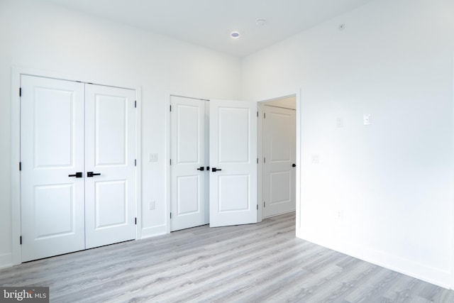 unfurnished bedroom featuring baseboards, light wood finished floors, and multiple closets