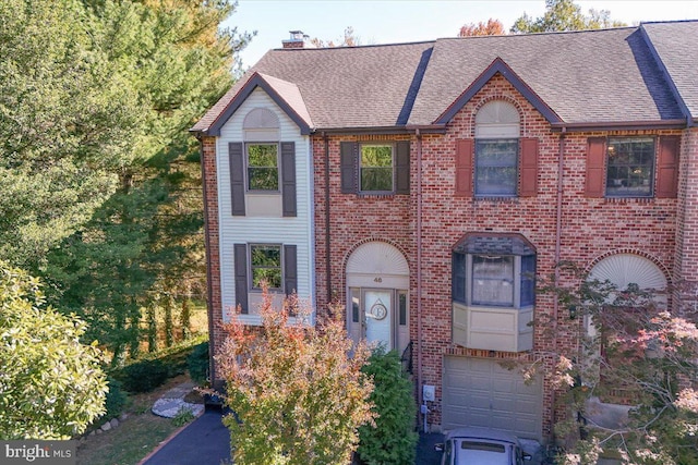 view of property featuring a garage, brick siding, a chimney, and a shingled roof