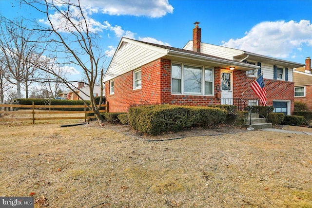 tri-level home featuring a front yard, brick siding, fence, and a chimney