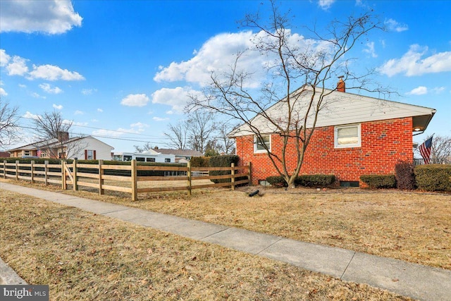 view of side of home featuring a chimney, fence, a lawn, and brick siding