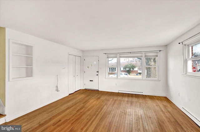 spare room featuring wood-type flooring, built in features, baseboard heating, and baseboards