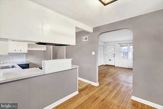 kitchen with visible vents, arched walkways, light wood-style flooring, white cabinetry, and backsplash