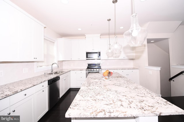 kitchen featuring stainless steel appliances, a sink, white cabinetry, a center island, and decorative light fixtures