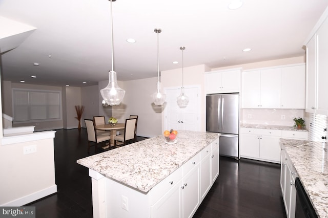 kitchen with a center island, white cabinetry, freestanding refrigerator, light stone countertops, and decorative light fixtures