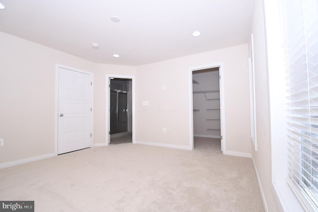 unfurnished bedroom featuring recessed lighting, light colored carpet, a spacious closet, and baseboards