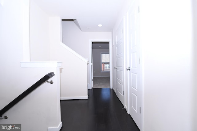 hallway with dark wood-style floors, baseboards, and an upstairs landing