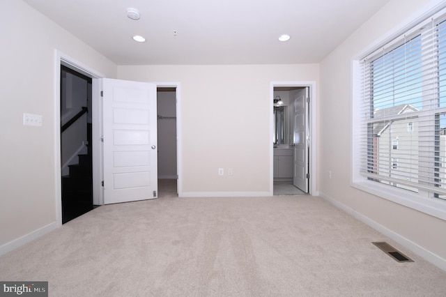 unfurnished bedroom featuring light carpet, baseboards, visible vents, and a walk in closet