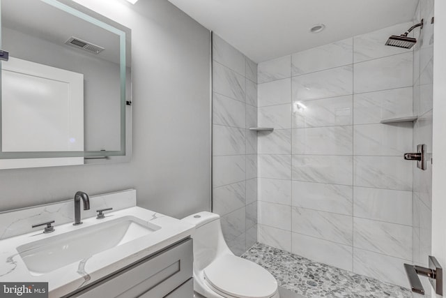 bathroom with toilet, visible vents, a tile shower, and vanity