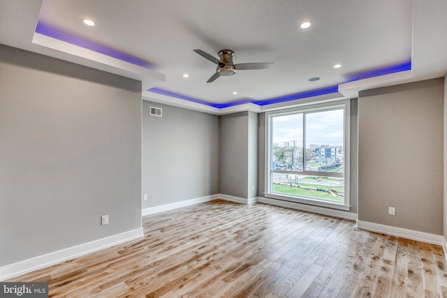 unfurnished room with baseboards, a raised ceiling, visible vents, and light wood-style floors