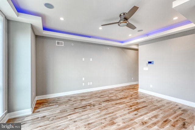 spare room with light wood-type flooring, visible vents, and a tray ceiling