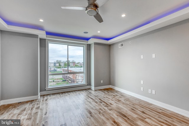 empty room with recessed lighting, visible vents, baseboards, light wood finished floors, and a raised ceiling