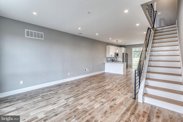 unfurnished living room with recessed lighting, visible vents, stairway, light wood-type flooring, and baseboards