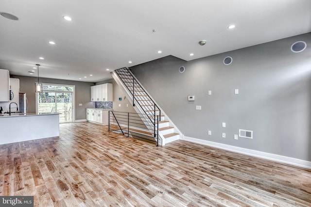 unfurnished living room with recessed lighting, visible vents, light wood-style flooring, a sink, and stairs