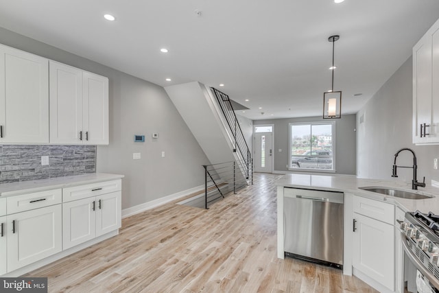 kitchen with stainless steel appliances, tasteful backsplash, white cabinetry, a sink, and light wood-type flooring