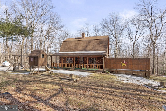 back of house featuring an outbuilding, covered porch, a shingled roof, a gambrel roof, and a shed