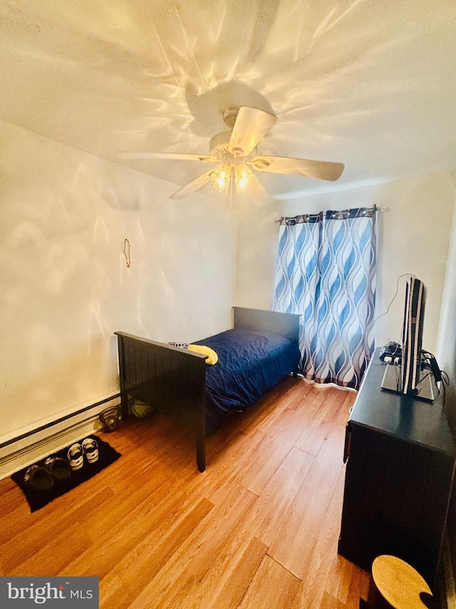 bedroom with a baseboard heating unit, ceiling fan, and wood finished floors