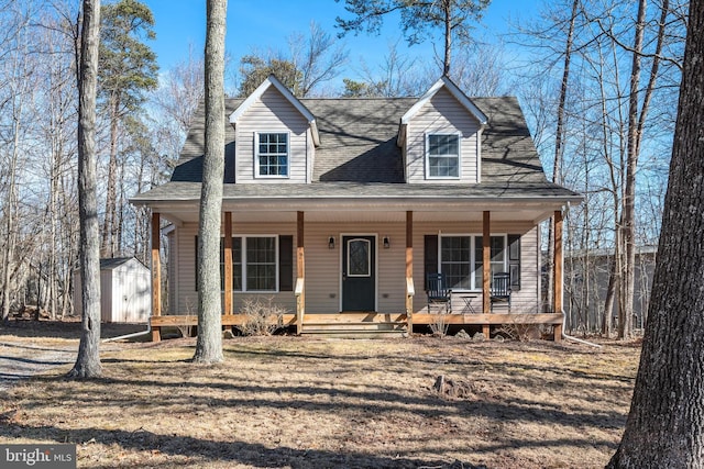 cape cod-style house with covered porch, roof with shingles, a storage unit, and an outdoor structure