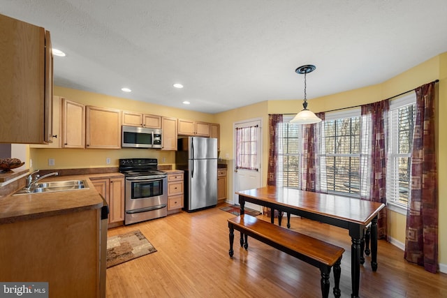 kitchen featuring light wood finished floors, dark countertops, appliances with stainless steel finishes, decorative light fixtures, and a sink